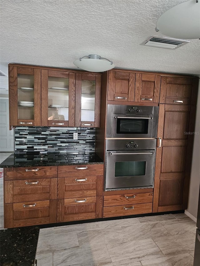 12215 Cobble Stone Dr, Hudson, FL 34667 - kitchen with double oven, brown cabinets, glass insert cabinets, dark stone countertops, and a textured ceiling