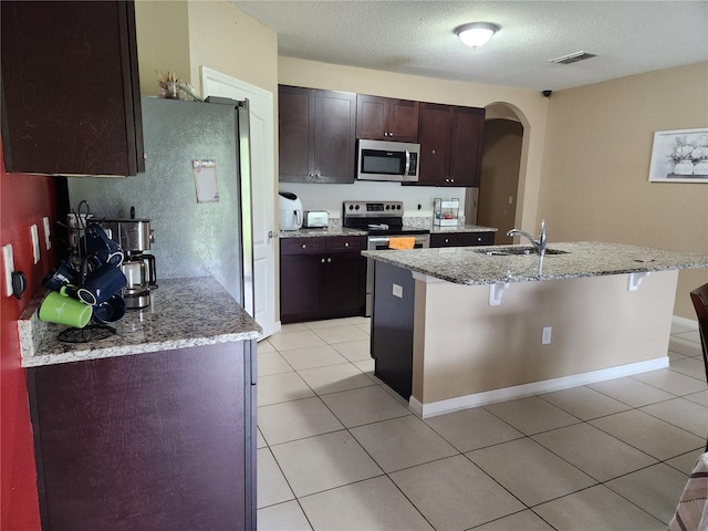 144 Hawthorne Way, Davenport, FL 33896 - kitchen featuring stainless steel appliances, arched walkways, an island with sink, a kitchen breakfast bar, and light stone countertops