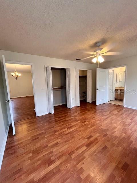 812 10th St, Saint Cloud, FL 34769 - unfurnished bedroom with a textured ceiling, multiple closets, a chandelier, wood finished floors, and ceiling fan