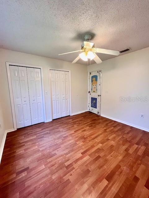 812 10th St, Saint Cloud, FL 34769 - unfurnished bedroom featuring wood finished floors, multiple closets, a textured ceiling, and a ceiling fan