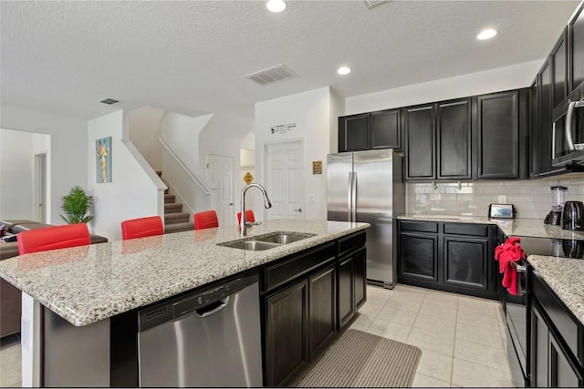 2231 Crofton Springs Ct, Davenport, FL 33837 - kitchen featuring appliances with stainless steel finishes, an island with sink, light stone counters, a textured ceiling, and open floor plan