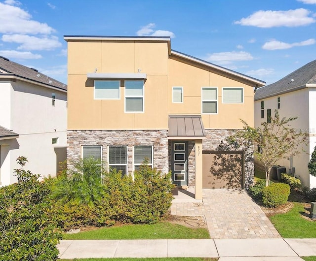 8937 Amelia Downs Trl, Kissimmee, FL 34747 - view of front facade with stone siding, stucco siding, a standing seam roof, an attached garage, and decorative driveway