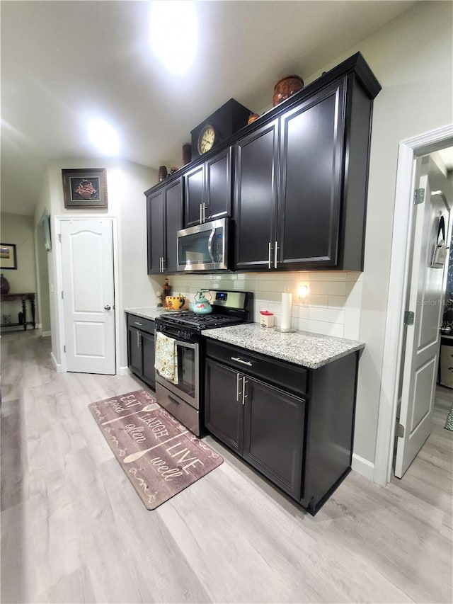 1456 Sourwood Dr, Ocoee, FL 34761 - kitchen with appliances with stainless steel finishes, tasteful backsplash, light wood-style floors, dark cabinetry, and light stone countertops