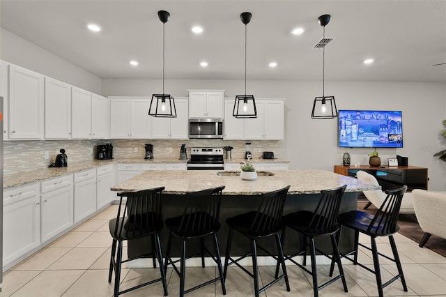 2131 Lelani Cir, Davenport, FL 33897 - kitchen with appliances with stainless steel finishes, decorative backsplash, light tile patterned flooring, white cabinets, and a center island with sink