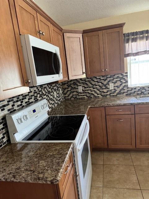 5435 Bryce Canyon Dr, Kissimmee, FL 34758 - kitchen with white appliances, light tile patterned floors, decorative backsplash, brown cabinetry, and a textured ceiling