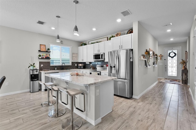 2436 Bulrush Dr, Saint Cloud, FL 34769 - kitchen featuring appliances with stainless steel finishes, light wood finished floors, a kitchen island, tasteful backsplash, and a textured ceiling