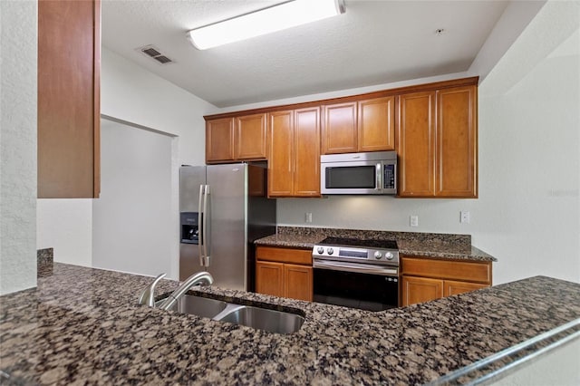 8309 Bella Vida Cir Unit 8309, Davenport, FL 33896 - kitchen with stainless steel appliances, dark stone countertops, brown cabinetry, and a textured ceiling