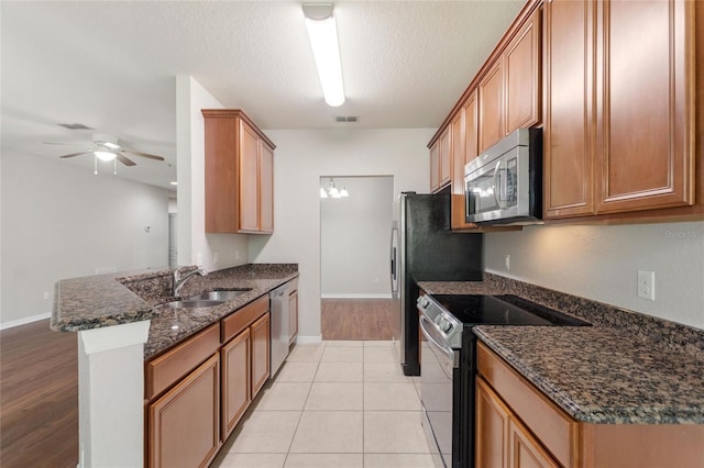 8309 Bella Vida Cir Unit 8309, Davenport, FL 33896 - kitchen with appliances with stainless steel finishes, a peninsula, a ceiling fan, dark stone countertops, and brown cabinets