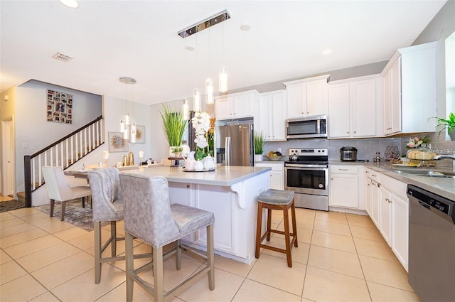 2463 Volunteer Ave, Kissimmee, FL 34744 - kitchen featuring appliances with stainless steel finishes, light tile patterned flooring, decorative backsplash, a kitchen island, and white cabinetry