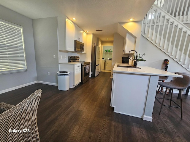 407 Darlington Loop, Davenport, FL 33896 - kitchen featuring stainless steel appliances, washer / clothes dryer, a breakfast bar area, dark wood-style flooring, and white cabinetry