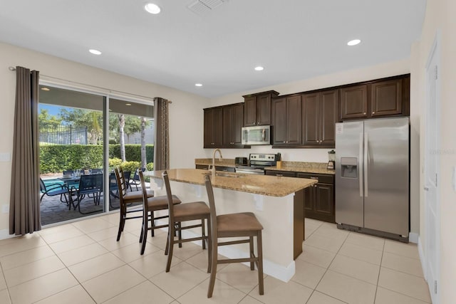 7403 Marker Ave, Kissimmee, FL 34747 - kitchen with appliances with stainless steel finishes, an island with sink, dark brown cabinetry, a breakfast bar area, and light stone countertops