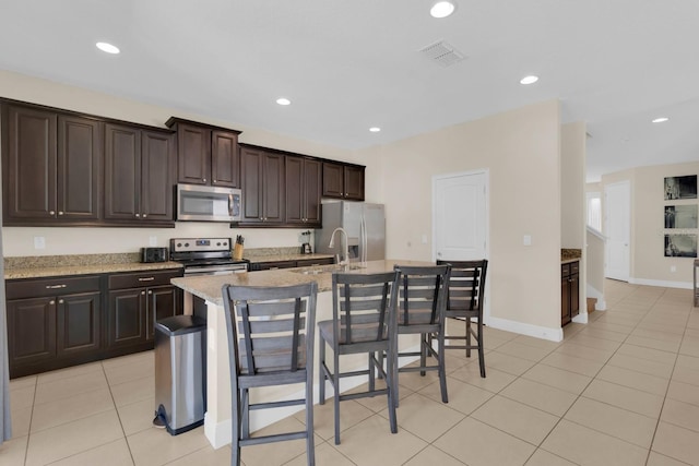 7403 Marker Ave, Kissimmee, FL 34747 - kitchen featuring appliances with stainless steel finishes, a kitchen island with sink, dark brown cabinetry, a kitchen breakfast bar, and recessed lighting