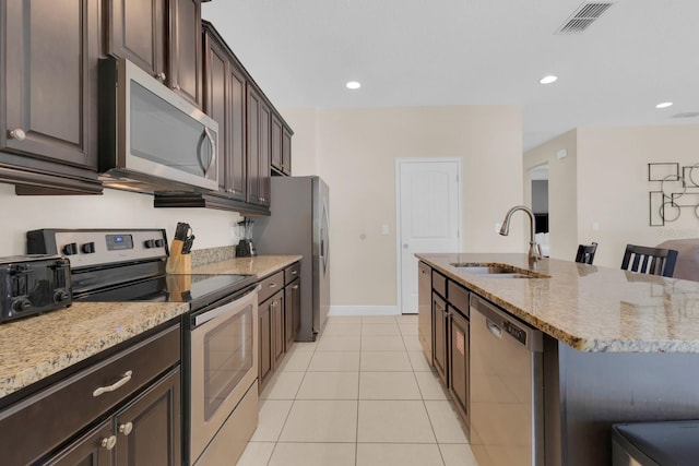 7403 Marker Ave, Kissimmee, FL 34747 - kitchen with appliances with stainless steel finishes, light tile patterned floors, light stone countertops, dark brown cabinetry, and a kitchen island with sink