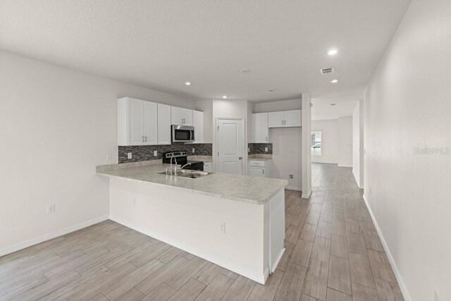 588 Meadow Bend Dr, Davenport, FL 33837 - kitchen with stainless steel appliances, a peninsula, light wood-style flooring, backsplash, and recessed lighting