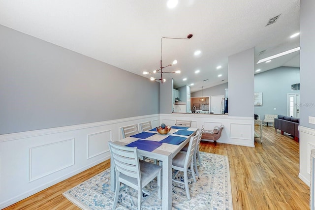 120 Bloomingdale Dr, Davenport, FL 33897 - dining space with light wood-style floors, a chandelier, a wainscoted wall, lofted ceiling, and a decorative wall