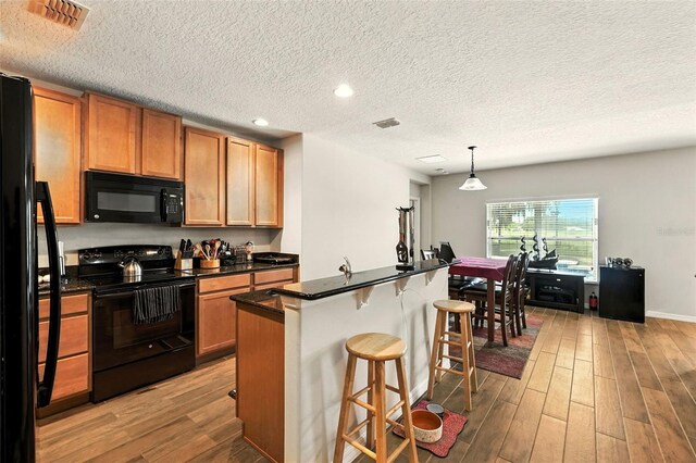 301 Sierra Way, Davenport, FL 33837 - kitchen featuring black appliances, light wood-style floors, a kitchen breakfast bar, dark countertops, and a textured ceiling