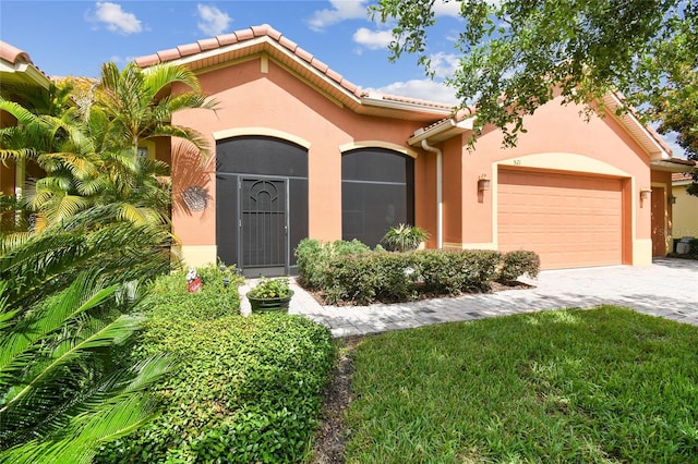 521 Milano Rd, Kissimmee, FL 34759 - mediterranean / spanish house featuring stucco siding, a tiled roof, an attached garage, decorative driveway, and a front lawn