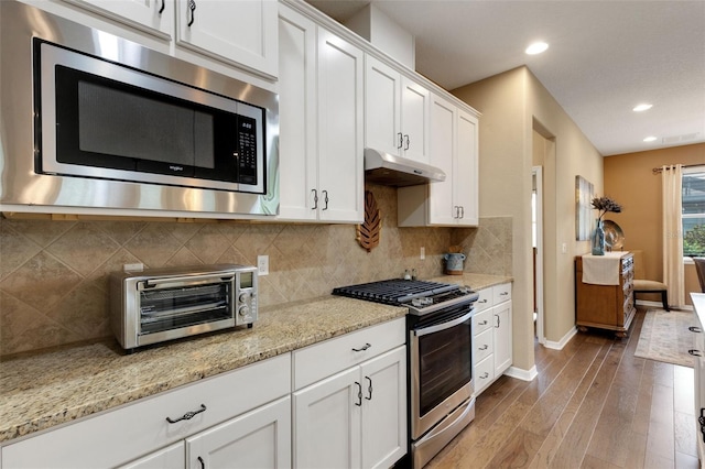802 Soria Ln, Davenport, FL 33837 - kitchen featuring appliances with stainless steel finishes, under cabinet range hood, wood finished floors, white cabinets, and light stone counters