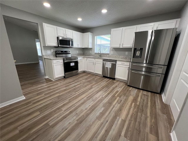 2211 Julianna Ct, Saint Cloud, FL 34769 - kitchen with appliances with stainless steel finishes, white cabinets, wood finished floors, recessed lighting, and light stone counters