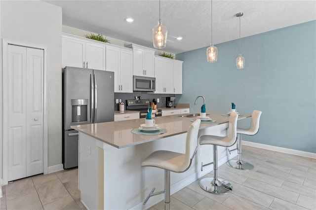 4840 Romeo Cir, Kissimmee, FL 34746 - kitchen featuring appliances with stainless steel finishes, a kitchen island with sink, white cabinetry, a breakfast bar, and decorative light fixtures