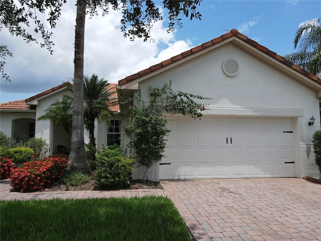 99 Auburn Dr, Kissimmee, FL 34759 - view of front of property featuring a tiled roof, a garage, stucco siding, and decorative driveway