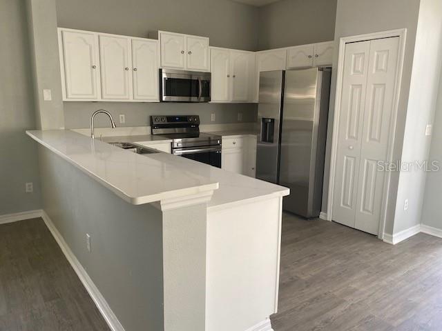 9048 Saint Andrews Way, Mount Dora, FL 32757 - kitchen featuring stainless steel appliances, a peninsula, wood finished floors, white cabinets, and light countertops