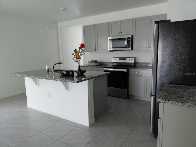 2132 Desert Rose Dr, Davenport, FL 33837 - kitchen featuring stainless steel appliances, light tile patterned flooring, gray cabinetry, dark stone countertops, and an island with sink