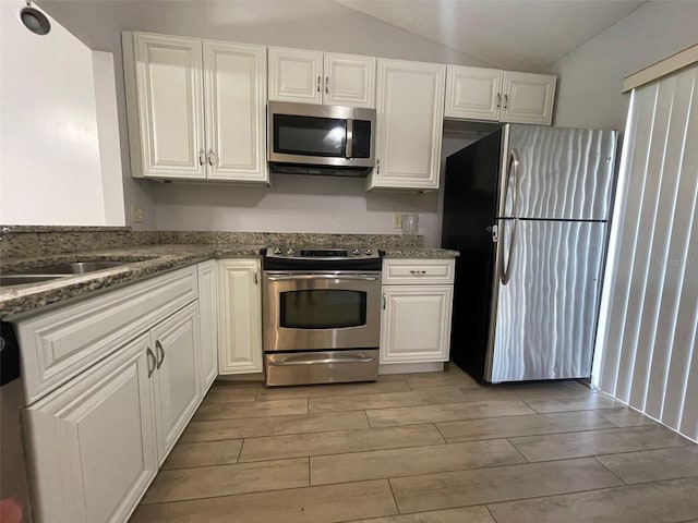 12161 Sandal Creek Way, Orlando, FL 32824 - kitchen with stainless steel appliances, vaulted ceiling, white cabinets, and wood finish floors
