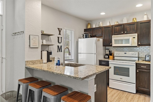 2602 Lodi Cir Unit 107, Kissimmee, FL 34746 - kitchen featuring white appliances, dark brown cabinetry, light wood-style flooring, a kitchen breakfast bar, and open shelves