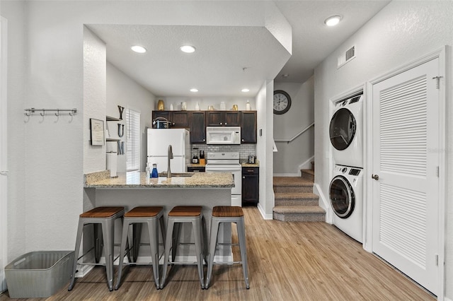 2602 Lodi Cir Unit 107, Kissimmee, FL 34746 - kitchen featuring white appliances, stacked washer / dryer, light wood finished floors, a breakfast bar area, and a peninsula