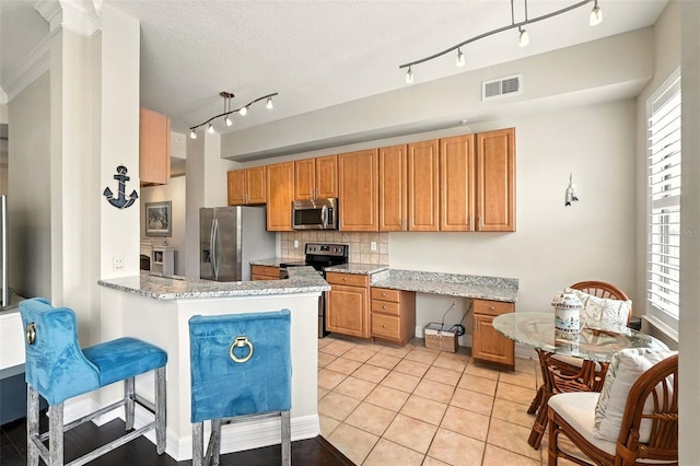 501 Mirasol Cir Unit 213, Celebration, FL 34747 - kitchen with appliances with stainless steel finishes, decorative backsplash, light stone countertops, a peninsula, and brown cabinetry