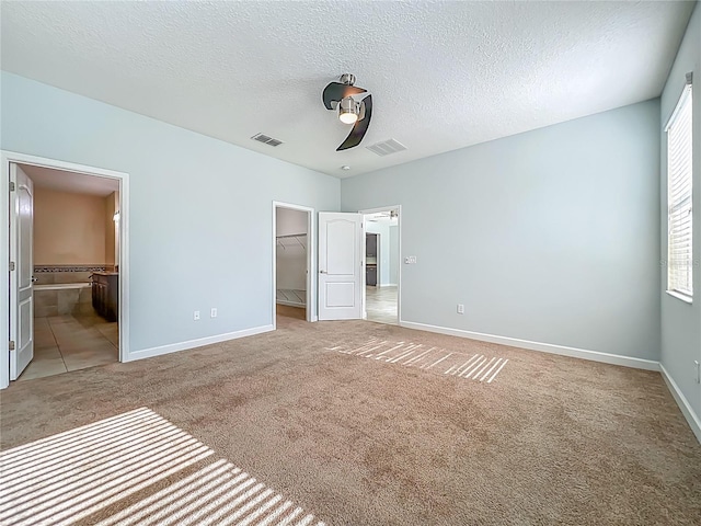 15150 Evergreen Oak Loop, Winter Garden, FL 34787 - unfurnished bedroom featuring light carpet, a walk in closet, a textured ceiling, ensuite bathroom, and ceiling fan