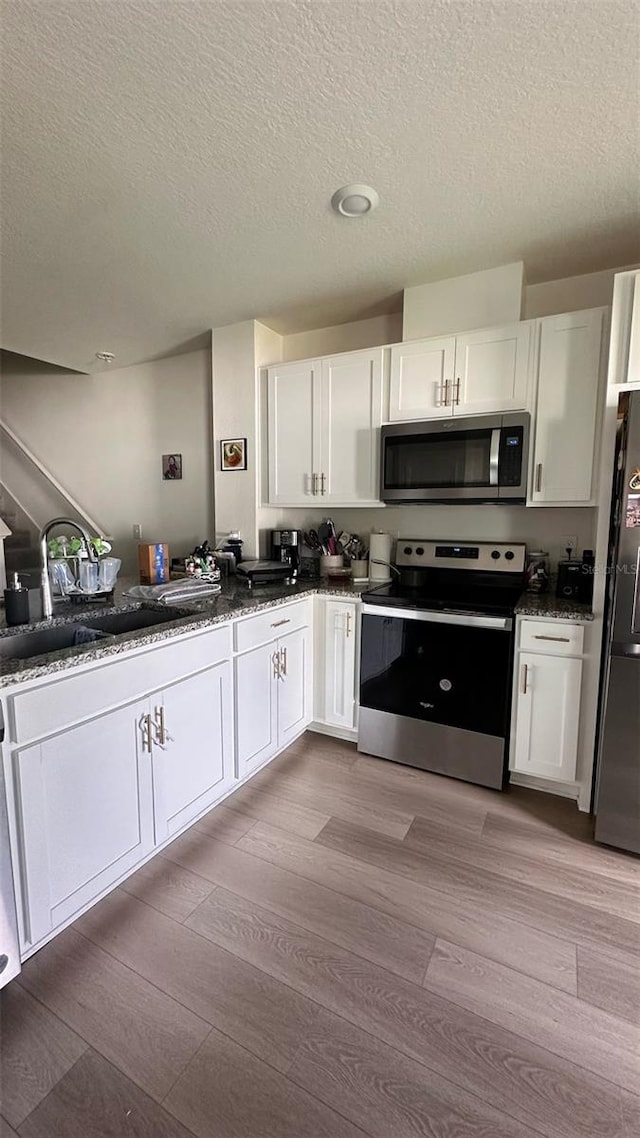 1528 Mirabella Cir, Davenport, FL 33897 - kitchen featuring stainless steel appliances, wood finished floors, white cabinets, a textured ceiling, and dark stone countertops