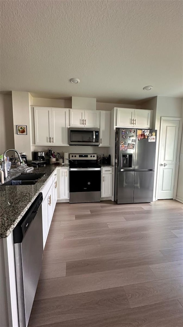 1528 Mirabella Cir, Davenport, FL 33897 - kitchen featuring stainless steel appliances, dark stone counters, white cabinets, light wood finished floors, and a textured ceiling