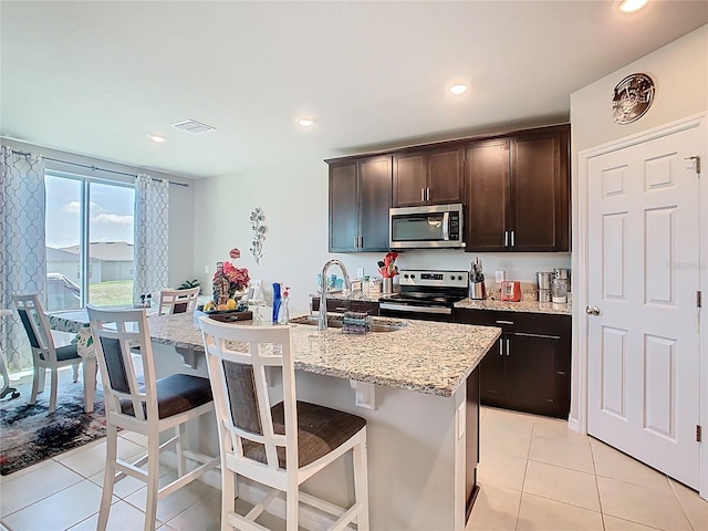 509 Mckenna Dr, Winter Haven, FL 33881 - kitchen featuring stainless steel appliances, light tile patterned flooring, dark brown cabinetry, a breakfast bar, and light stone counters