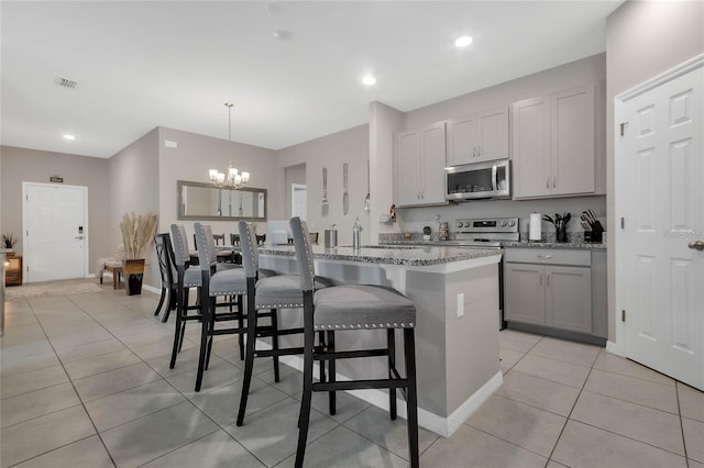 2661 Grasmere View Pkwy, Kissimmee, FL 34746 - kitchen featuring stainless steel appliances, a chandelier, light tile patterned flooring, light stone counters, and a center island with sink