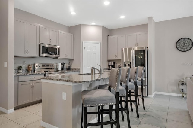 2661 Grasmere View Pkwy, Kissimmee, FL 34746 - kitchen with appliances with stainless steel finishes, gray cabinets, light tile patterned flooring, a kitchen breakfast bar, and light stone counters