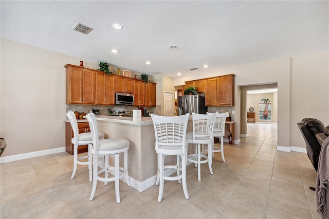 143 Tiger Lily Ct, Davenport, FL 33837 - kitchen with appliances with stainless steel finishes, brown cabinets, backsplash, a kitchen bar, and light countertops