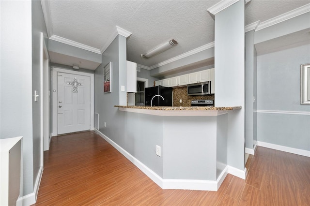 5548 Metrowest Blvd Unit 202, Orlando, FL 32811 - kitchen with appliances with stainless steel finishes, white cabinetry, light wood-style flooring, decorative backsplash, and crown molding