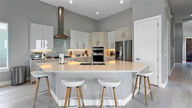 7551 Excitement Dr, Reunion, FL 34747 - kitchen with stainless steel appliances, wall chimney exhaust hood, a large island with sink, light wood-type flooring, and a towering ceiling