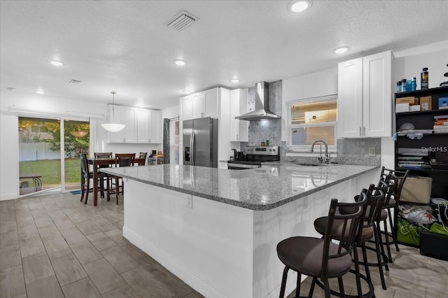 1208 Old Apopka Rd, Apopka, FL 32703 - kitchen featuring wall chimney exhaust hood, appliances with stainless steel finishes, a peninsula, light stone countertops, and white cabinets