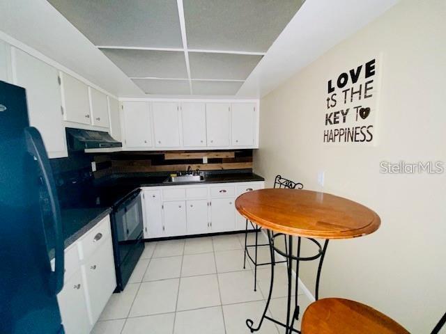221 Columbia Dr Unit 342, Cape Canaveral, FL 32920 - kitchen with refrigerator with ice dispenser, black range with electric stovetop, dark countertops, light tile patterned floors, and white cabinets