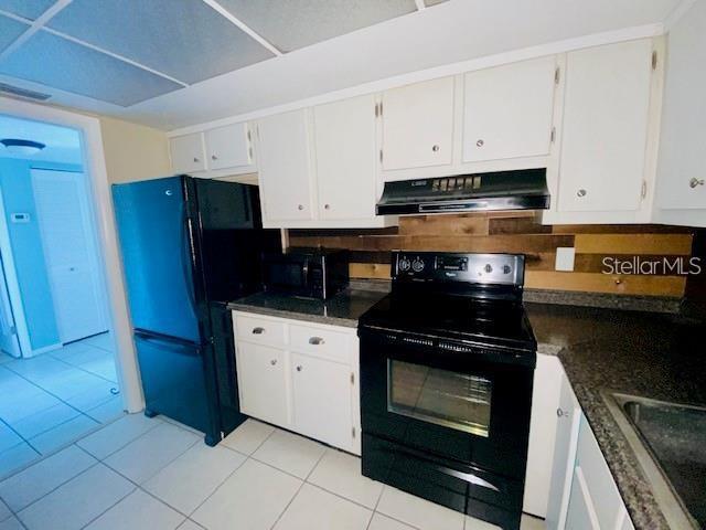 221 Columbia Dr Unit 342, Cape Canaveral, FL 32920 - kitchen with black appliances, backsplash, ventilation hood, white cabinets, and light tile patterned flooring