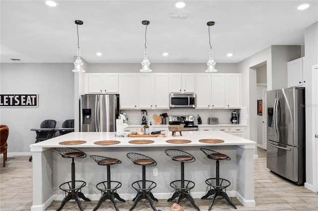 2541 Shanti Dr, Kissimmee, FL 34746 - kitchen featuring stainless steel appliances, light wood-style floors, decorative backsplash, a kitchen bar, and white cabinetry