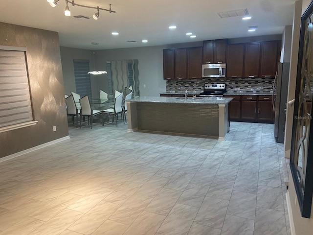 2618 San Simeon Way, Kissimmee, FL 34741 - kitchen featuring stainless steel appliances, backsplash, light stone counters, dark brown cabinets, and a kitchen island with sink