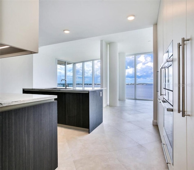 kitchen with oven, a kitchen island with sink, sink, dark brown cabinetry, and a water view