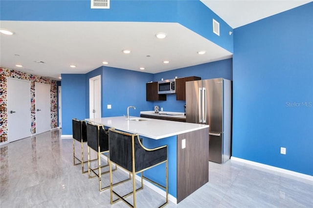 kitchen with dark brown cabinets, a kitchen bar, stainless steel appliances, sink, and a center island with sink