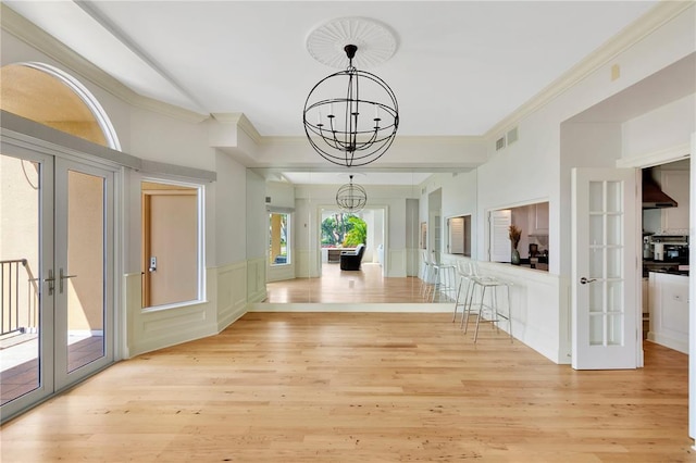 interior space featuring an inviting chandelier, crown molding, french doors, and light wood-type flooring