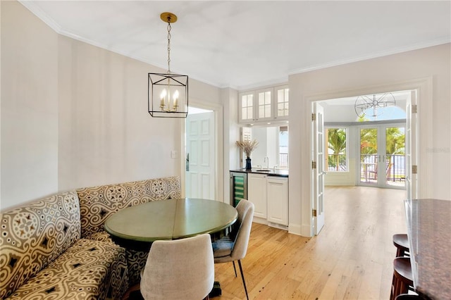 dining space with ornamental molding, light hardwood / wood-style floors, a notable chandelier, and french doors