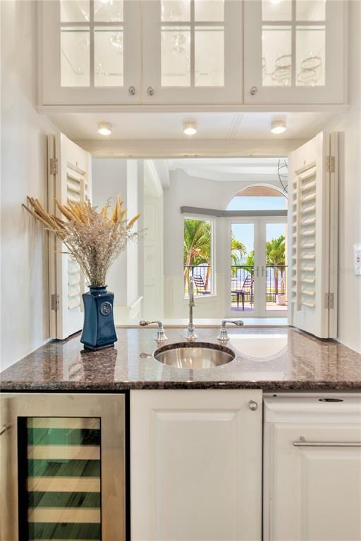 bar with beverage cooler, dark stone countertops, white cabinetry, and sink